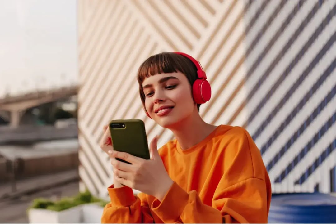 girl-orange-sweatshirt-listening-music-striped-backdrop