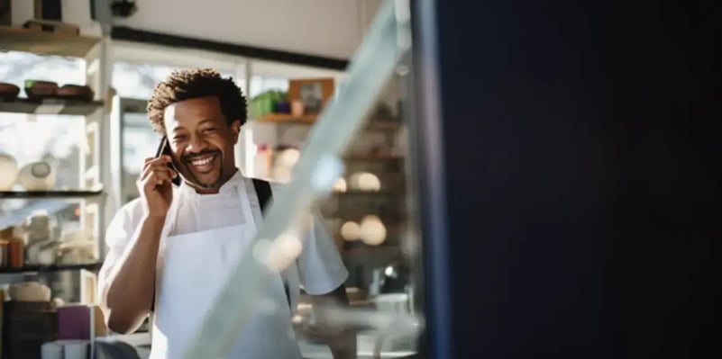 man-in-a-white-apron-and-shirt-smiling-and-talking-on-the-phone