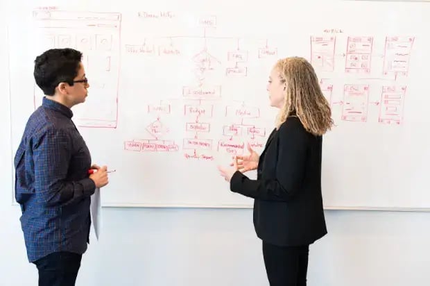 two-women-standing-in-front-of-whiteboard